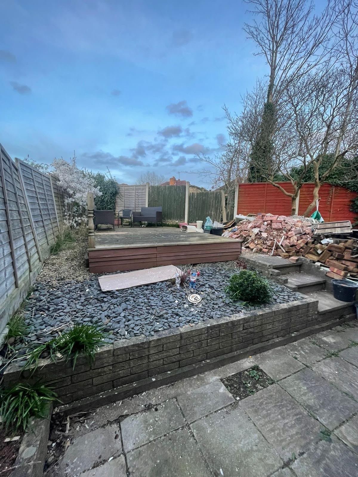 Back garden before the work: stained concrete slabs, slate chippings, an old deck and a pile of brick rubble