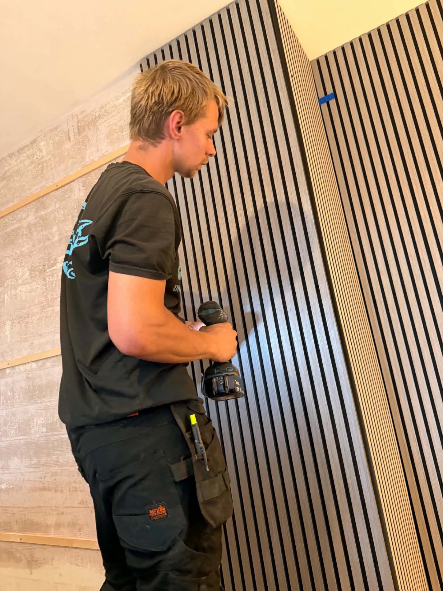 Ozz drilling vertical wooden slat panels into place over timber battens on an interior feature wall