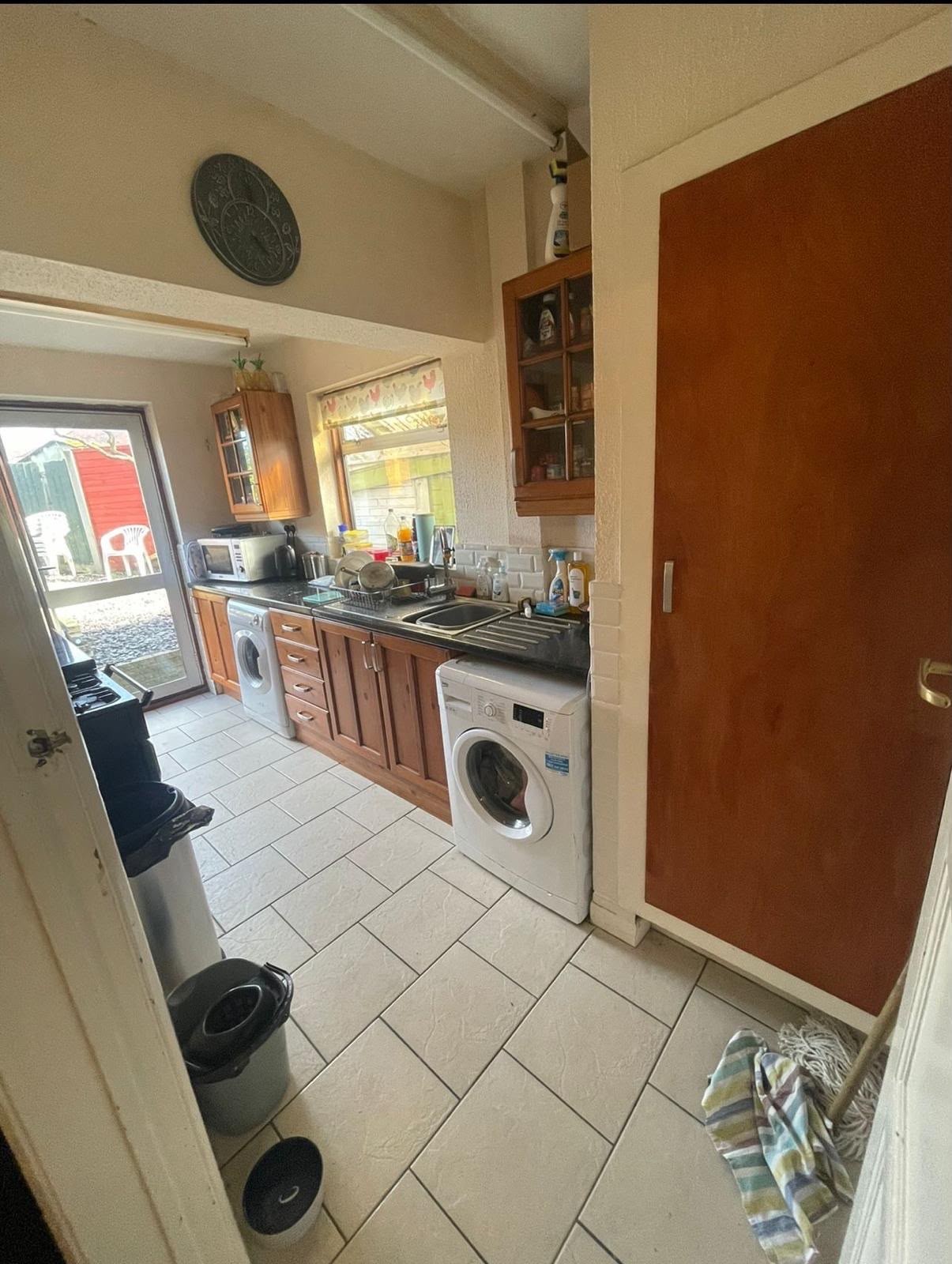 Kitchen before the fit out: dated pine cabinets, dark laminate worktops, exposed washing machines and beige floor tiles