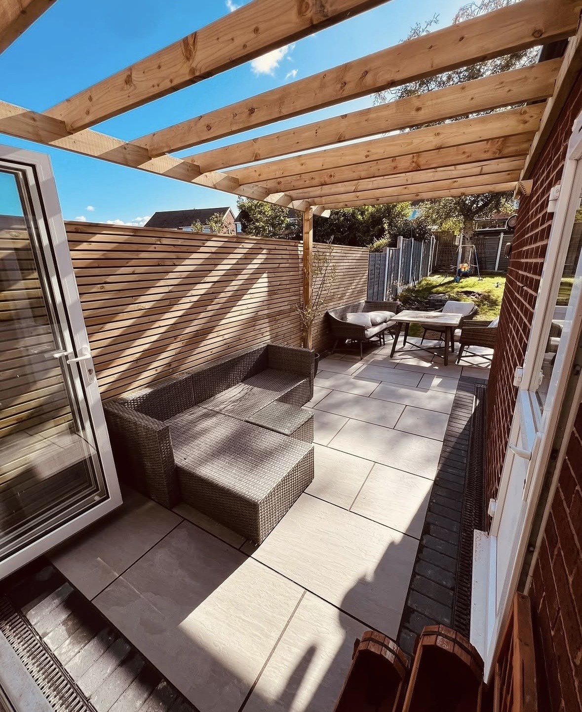 The same garden after the work: porcelain paving, a timber pergola, a slatted privacy screen and outdoor lounge furniture