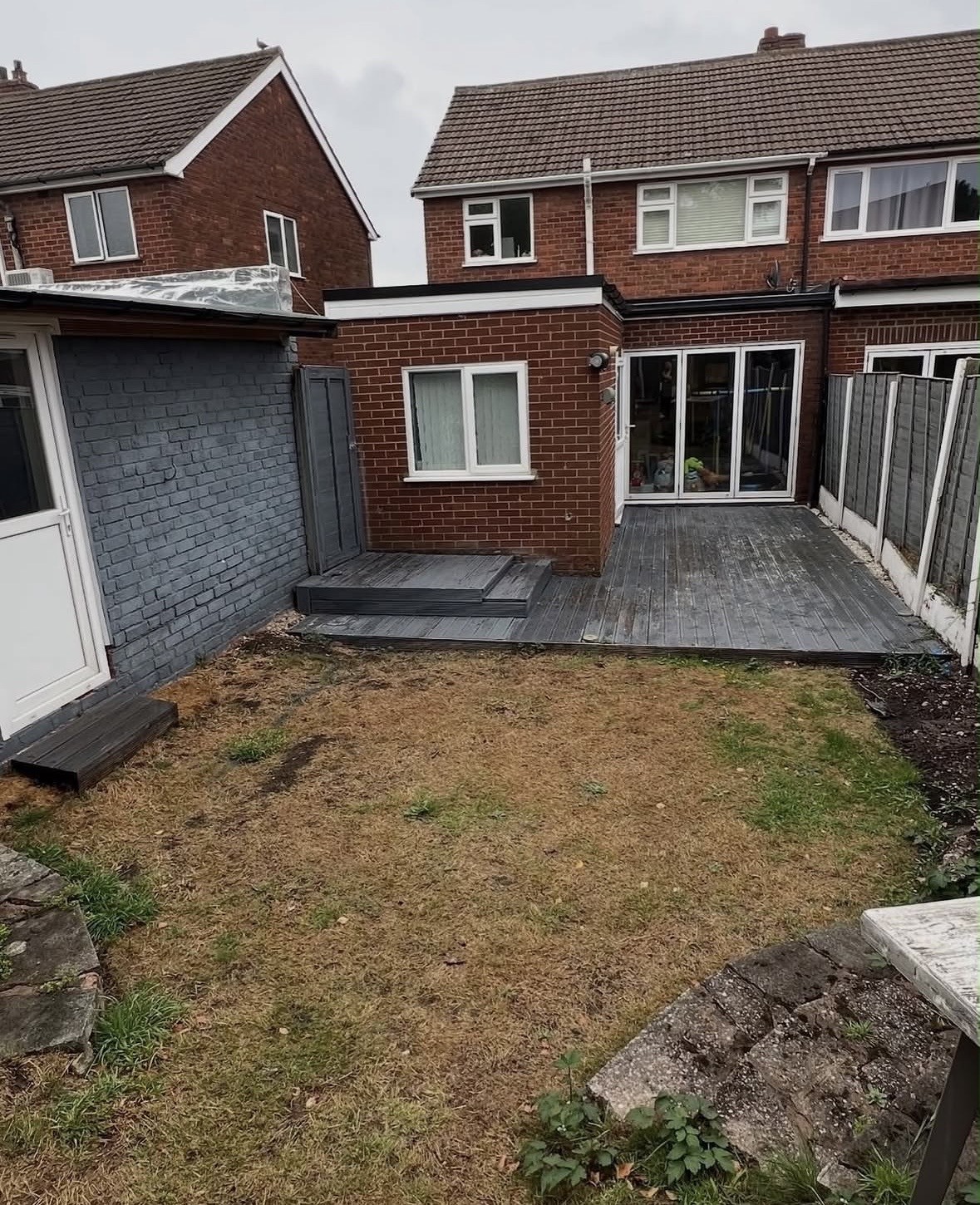Garden before the work: patchy dead lawn, weathered grey decking and a bare brick extension